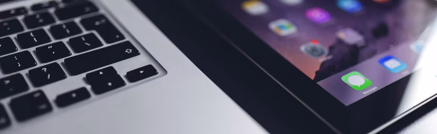Close-up of a laptop and an iPad showing its app icons, on a dark background