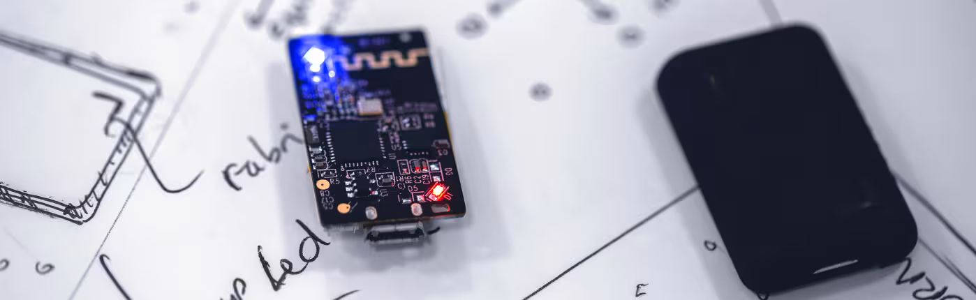 Small electronic board with a blue LED on a sheet of sketches, next to a black case