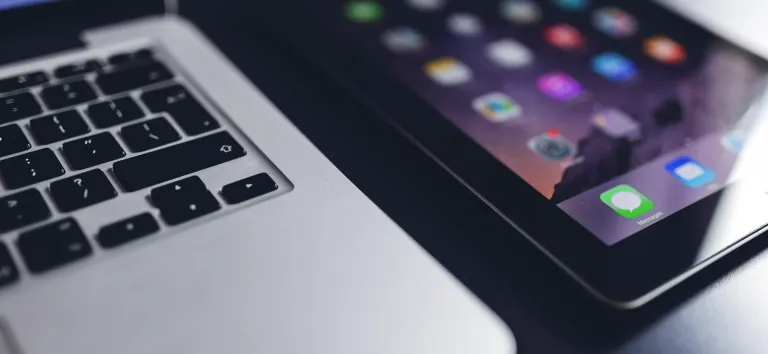 Close-up of a laptop and an iPad showing its app icons, on a dark background