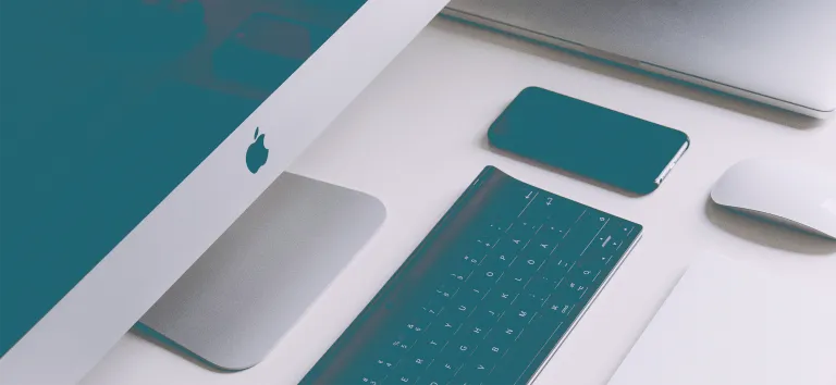 iMac, clavier et iPhone teintés bleu sarcelle sur un bureau blanc, une souris à droite