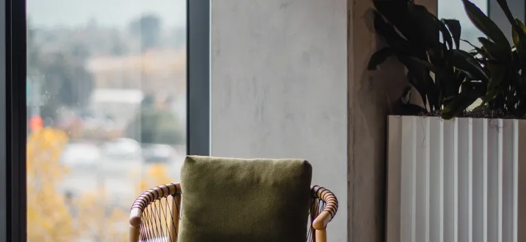Armchair and wooden coffee table by a large window, a concrete wall and a plant