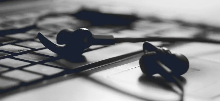 Black earphones resting on a laptop keyboard, in black and white