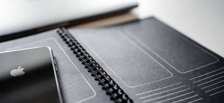 Black spiral notebook with screen templates drawn in it, a smartphone lying on it