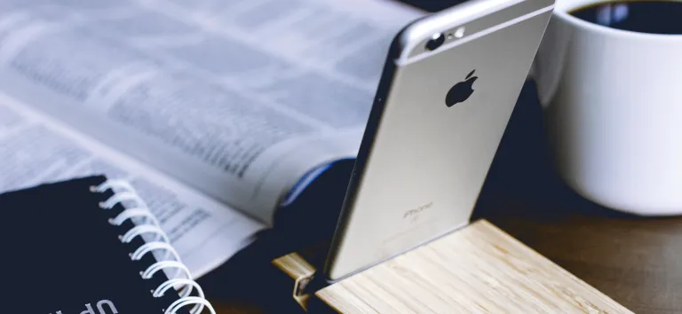 Open newspaper, spiral notebook, smartphone on a wooden stand and a cup of coffee