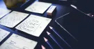 Croquis de maquettes d’écrans sur des fiches, crayons et smartphone sur un bureau sombre
