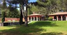 Maison de vacances aux murs rouges et à arcades, pelouse et pins, sous le soleil