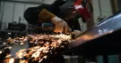 Ouvrier casqué meulant une poutre métallique, une gerbe d’étincelles jaillit