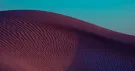 Crête d’une dune striée par le vent, rose et violette, sous un ciel turquoise