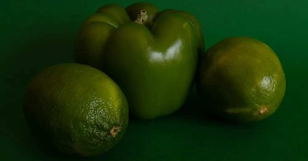 A green pepper and two limes on a green background