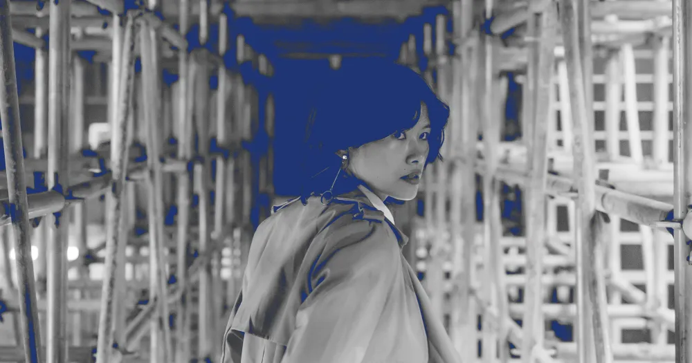 Young woman in a coat among scaffolding, black-and-white photo with blue accents