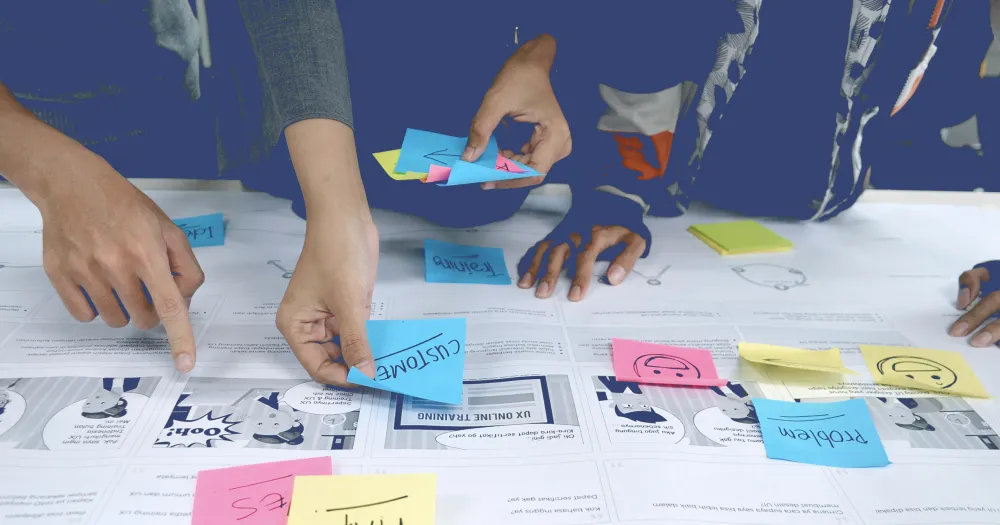 Mains posant des notes adhésives colorées sur des maquettes imprimées pendant un atelier