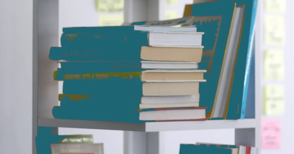 Pile de livres aux couvertures bleu sarcelle sur une étagère blanche, des notes adhésives au mur