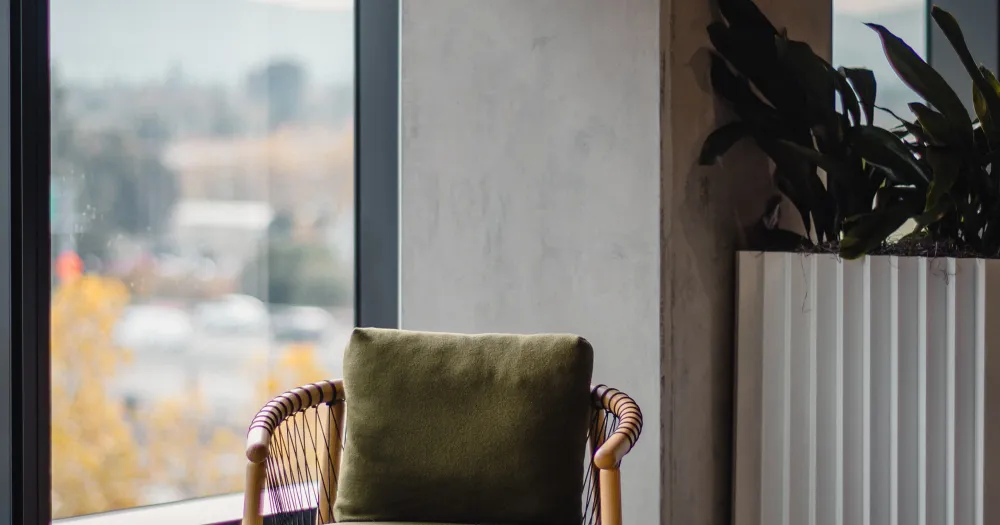 Fauteuil et table basse en bois près d’une baie vitrée, un mur de béton et une plante