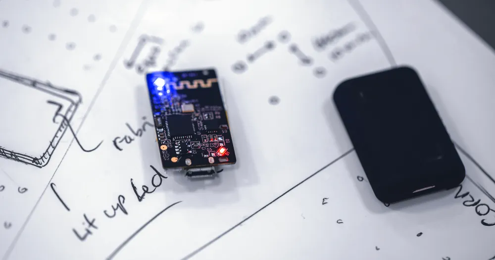Small electronic board with a blue LED on a sheet of sketches, next to a black case