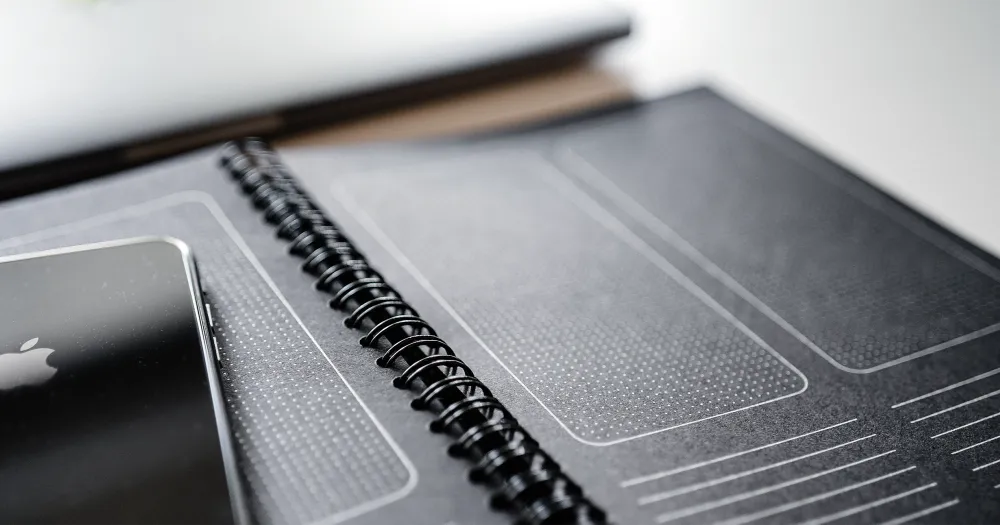 Black spiral notebook with screen templates drawn in it, a smartphone lying on it