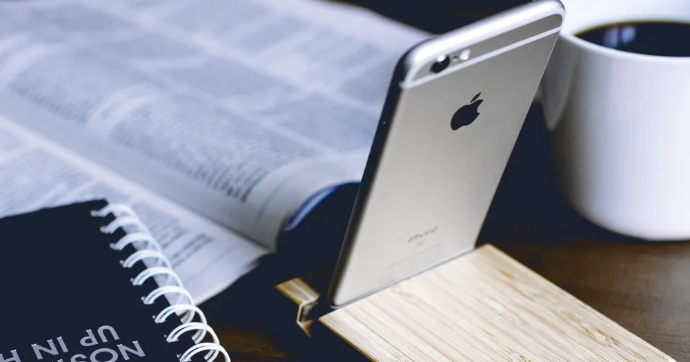 Open newspaper, spiral notebook, smartphone on a wooden stand and a cup of coffee