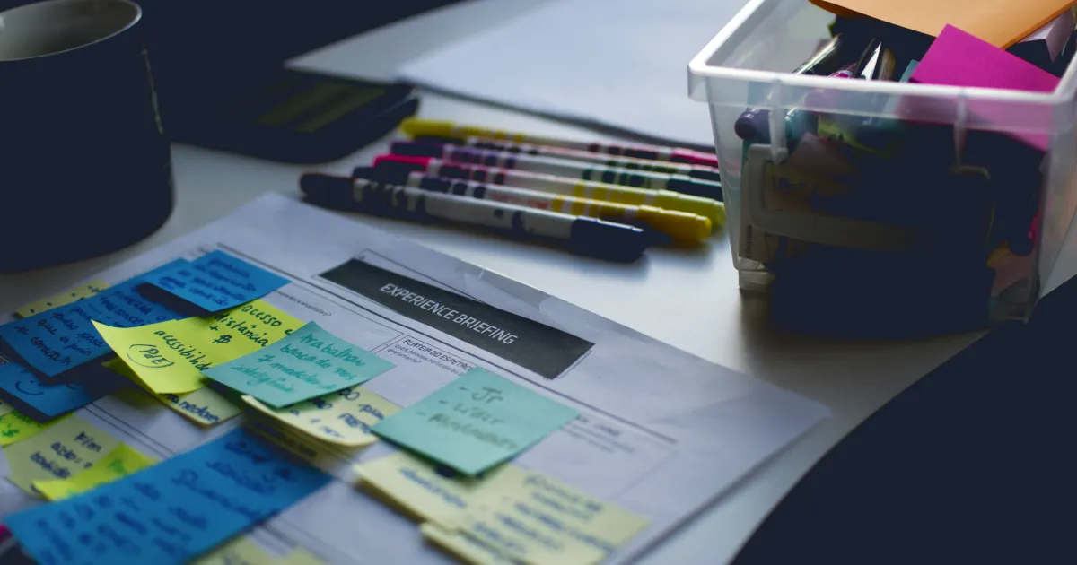 Colourful sticky notes on a worksheet, markers and a box of supplies on a desk