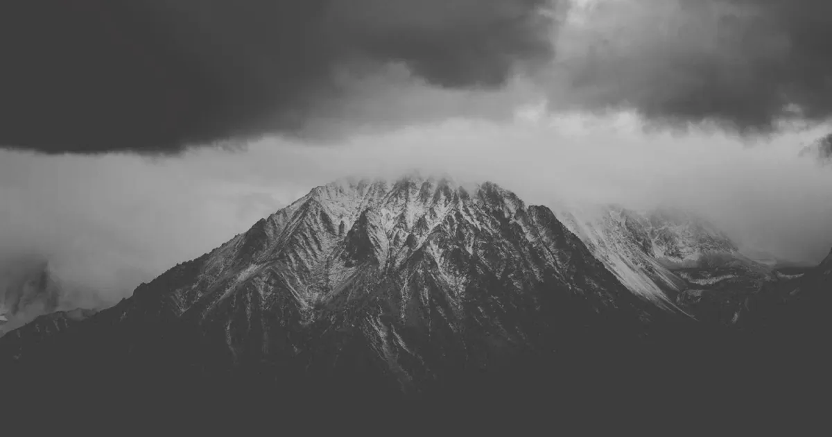 Sommet enneigé sous des nuages d’orage, en noir et blanc