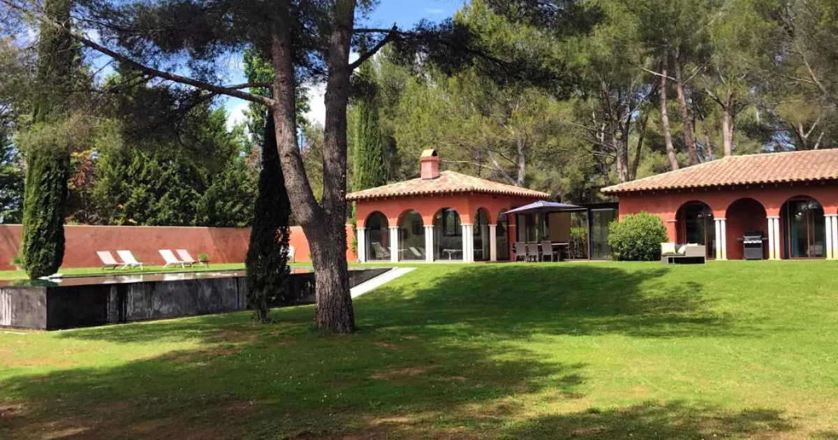 Maison de vacances aux murs rouges et à arcades, pelouse et pins, sous le soleil