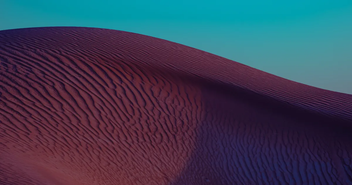 Crête d’une dune striée par le vent, rose et violette, sous un ciel turquoise